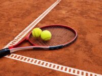 Tennis,Racket,With,Two,Balls,On,Clay,Court